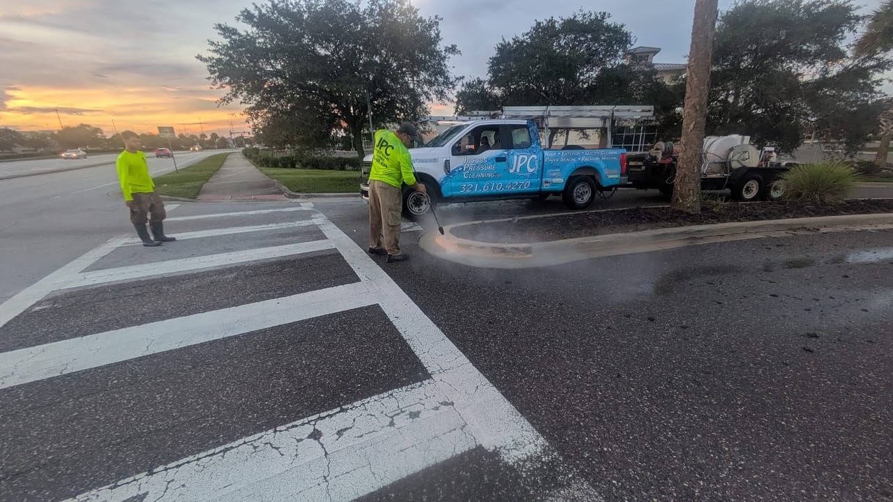 JPC crew surface-cleaning a crosswalk and curb line at Hammock Landing shopping plaza at sunrise